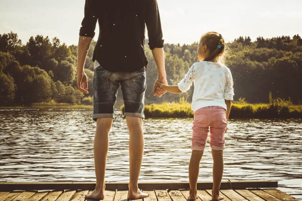A father and his daughter hold hands on a dock.