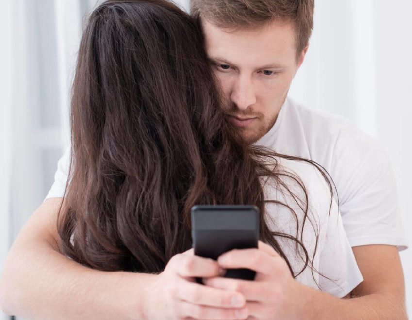 The role of social media in divorce cases. Man writing on his phone, while hugging wife.