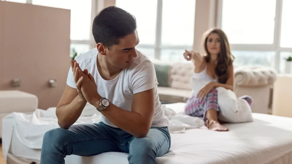 A couple sitting on a bed, arguing about the filing of an at-fault divorce.
